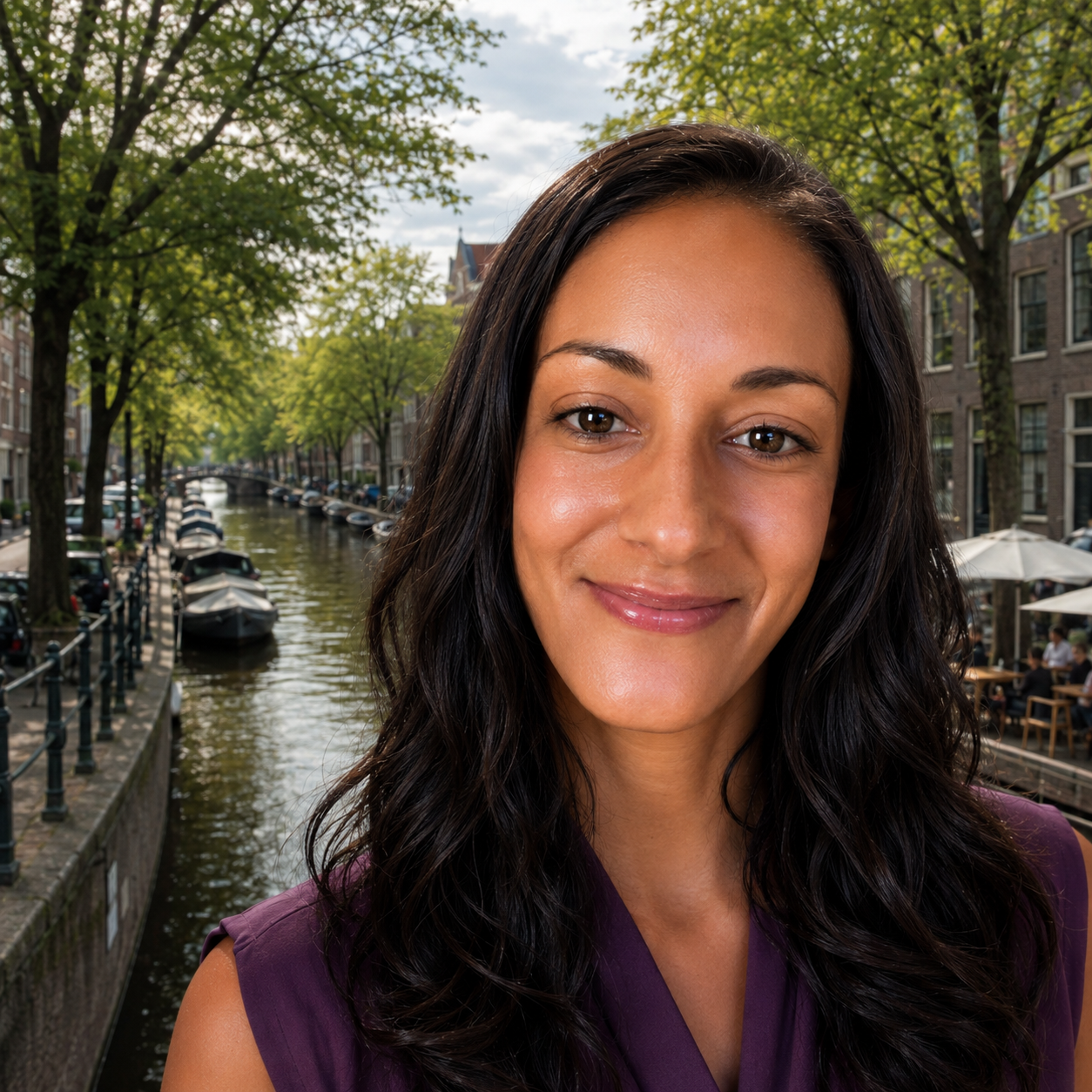 La Dra. Elizabeth Rojas, sonriente, de pie frente a un canal bordeado de árboles con barcas amarradas